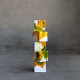 Five gourmet chocolate truffles in white, yellow, and green artfully stacked on top of one another in front of a concrete background.