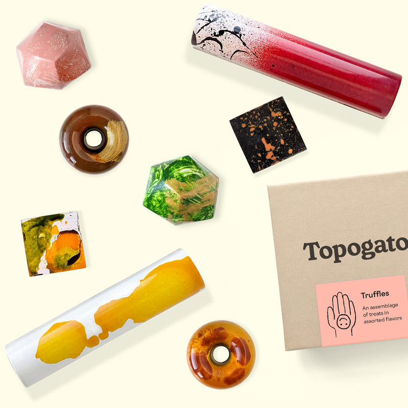 A colorful arrangement of gourmet chocolate bars and dark chocolate truffles. Sweet treats shown from the top down, alongside a branded gift box from online chocolate store Topogato.