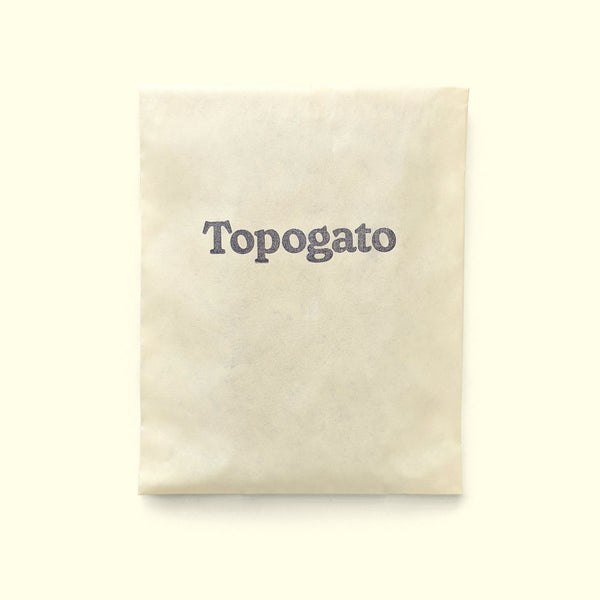 A handmade chocolate bar wrapped up for chocolate delivery in a cream sleeve with a logo of gourmet chocolate company Topogato shown from the top down.